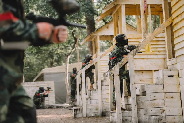屋外のペイント ボール銃で木製の塔の階段の上に立って制服と防護マスクのペイント ボール チーム  — 無料ストックフォト