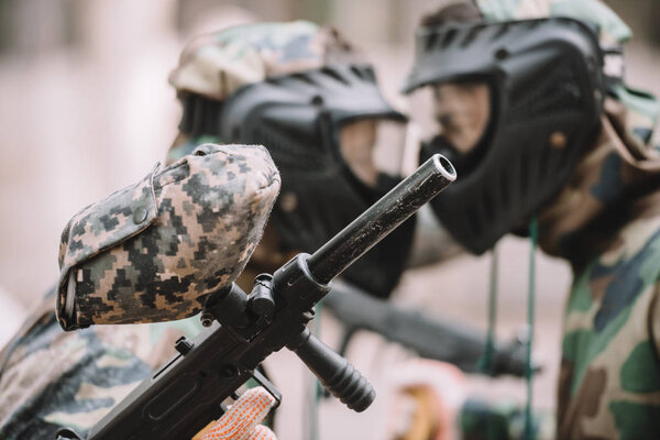 selective focus of marker gun in hand of paintball player standing face to face with other player outdoors 