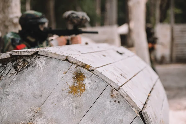 Selective Focus Paintball Splashes Wooden Barrel Paintball Player Shooting Outdoors — Free Stock Photo