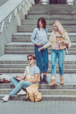 women brought coffee to go for friend on city steps in new city clipart