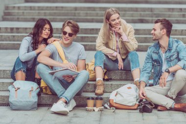 young tourists resting on steps on street of new city clipart