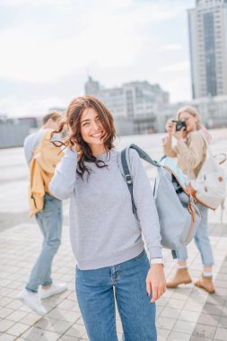 cheerful brunette girl walking with friends in city clipart