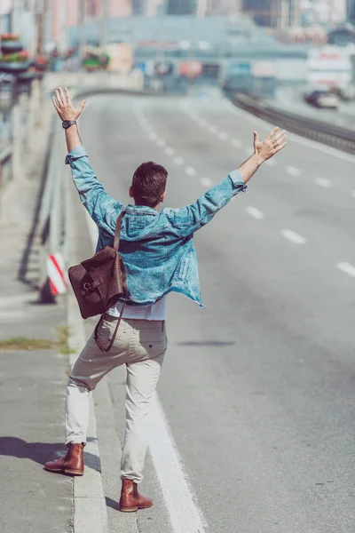 back view of man hitchhiking alone on road