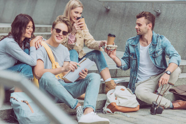 Молодые туристы с кофе отдыхают на ступеньках по улице нового города
