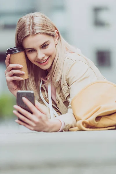 スマート フォンで Selfie 取りにコーヒーで陽気な金髪女の子 — ストック写真