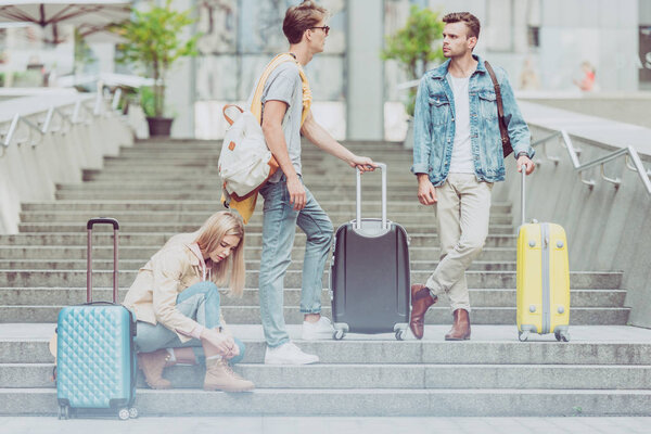 young stylish tourists with backpacks and travel bags on stairs in city