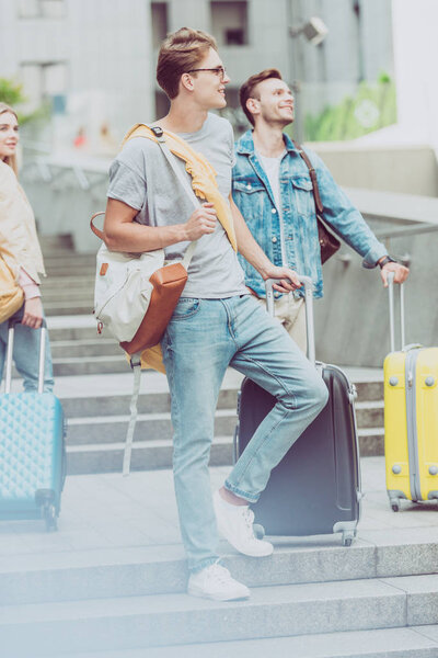 young stylish friends with backpacks and travel bags on stairs