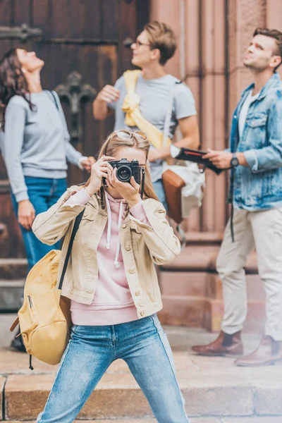 girl taking photo of city on camera with friends behind