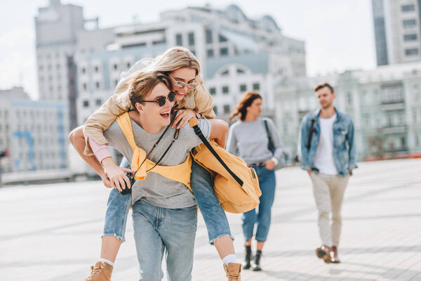 happy couple having fun and piggybacking in city with friends behind