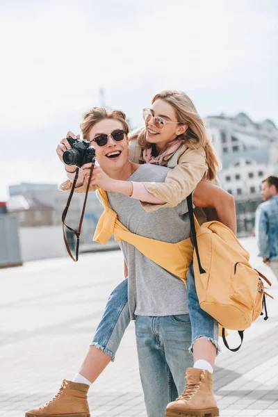 愉快的男朋友给背着带相机在城市的女朋友 — 图库照片