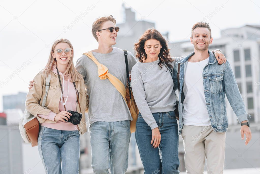 young cheerful friends hugging and walking in urban city