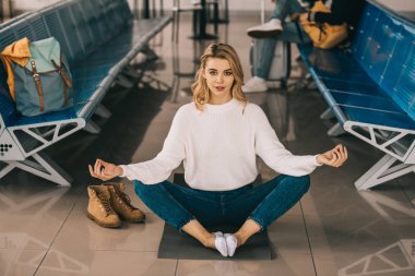 kız meditasyon Lotus pozisyonu ve havaalanı terminal bekleyen uçuş sırasında kamera bakıyor 