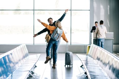 happy young friends with backpacks greeting each other in airport clipart