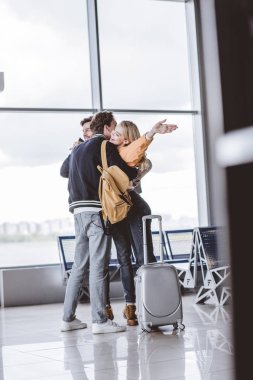 happy young friends hugging and greeting each other in airport clipart