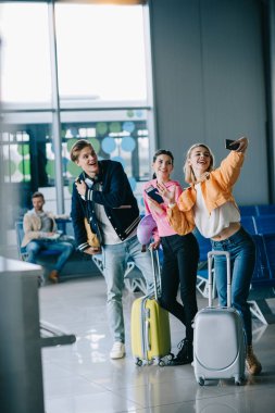 happy young friends taking selfie with smartphone in airport clipart