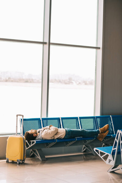 young man lying on seats while waiting for flight in airport terminal 