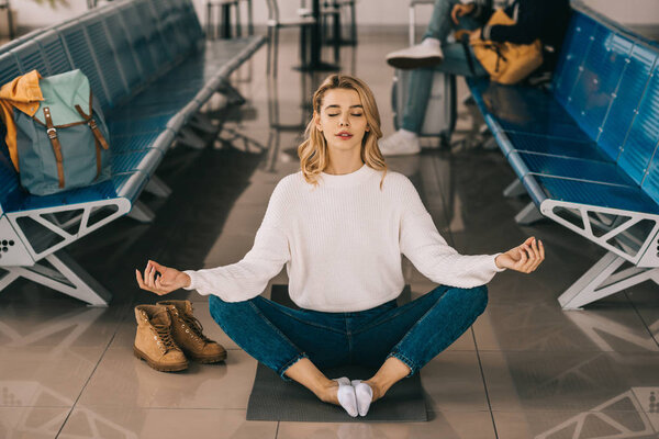 девушка медитирует в позе лотоса во время ожидания полета в терминале аэропорта
  