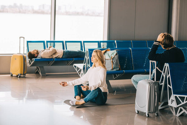 young woman meditating in lotus position while waiting flight in airport terminal