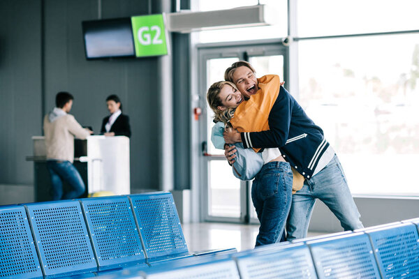 счастливые юноша и девушка обнимаются в аэропорту
