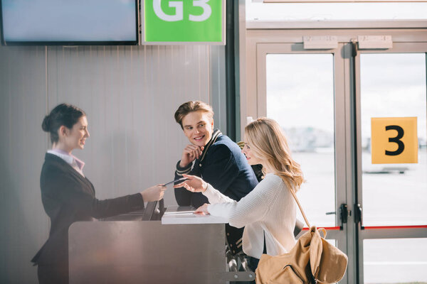 вид сбоку улыбающейся молодой пары у стойки регистрации в аэропорту
 