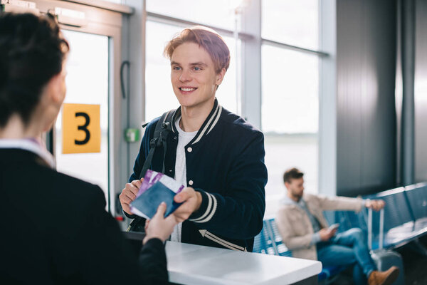 cropped shot of smiling man giving passport to airport staff