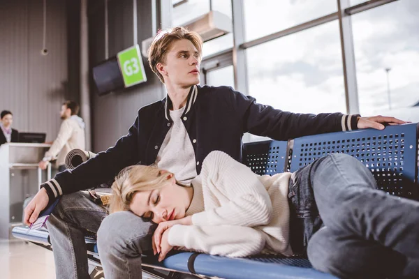 女孩睡觉和年轻人在等待航班在机场航站楼外寻找 — 图库照片