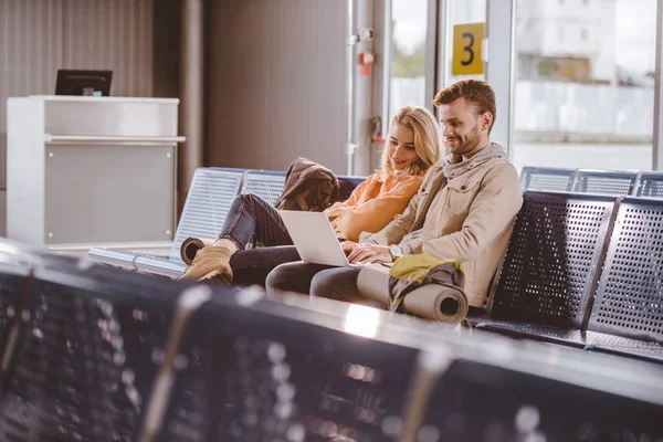 Uśmiechnięta Młoda Para Pomocą Laptopa Czekając Lot Lotnisko — Darmowe zdjęcie stockowe