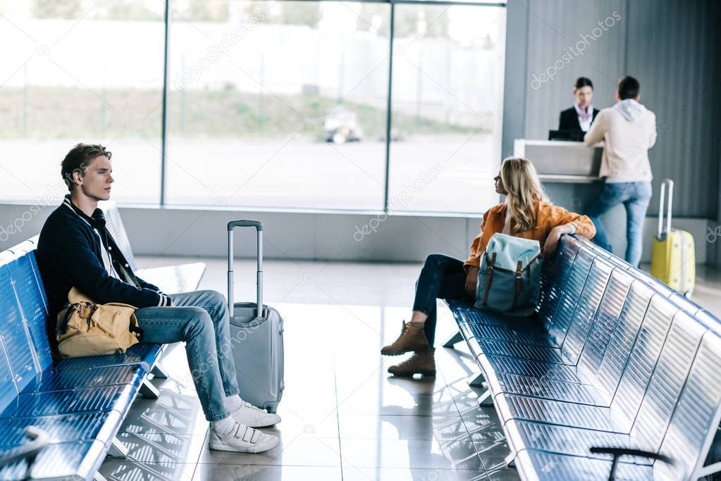 young people with luggage sitting and waiting for flight in airport terminal