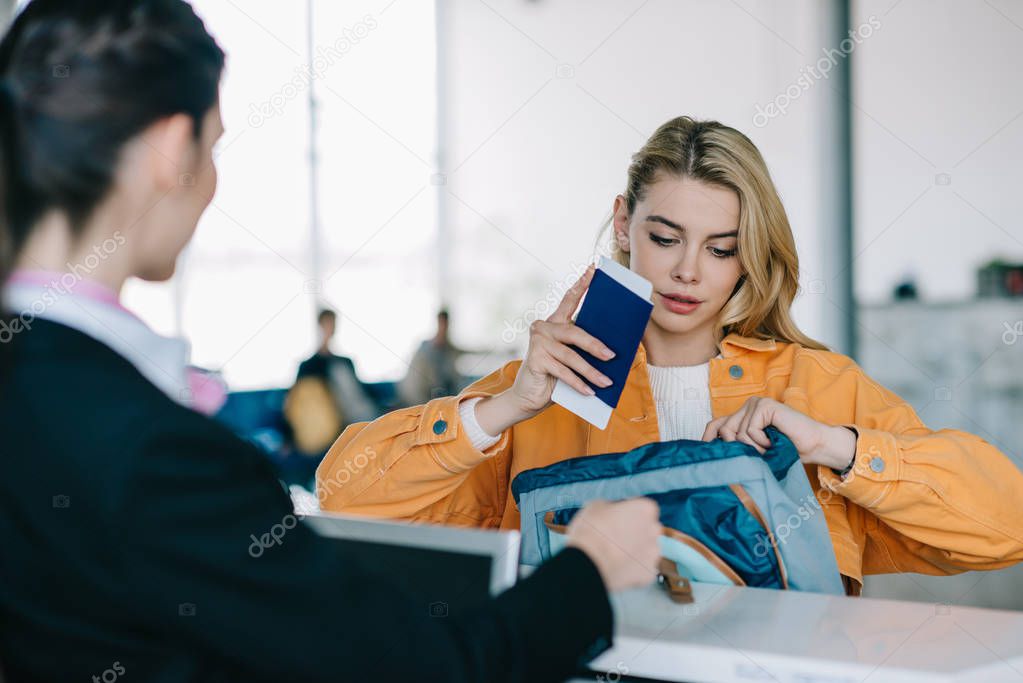 young woman putting passport with boarding pass into bag at check-in desk in airport