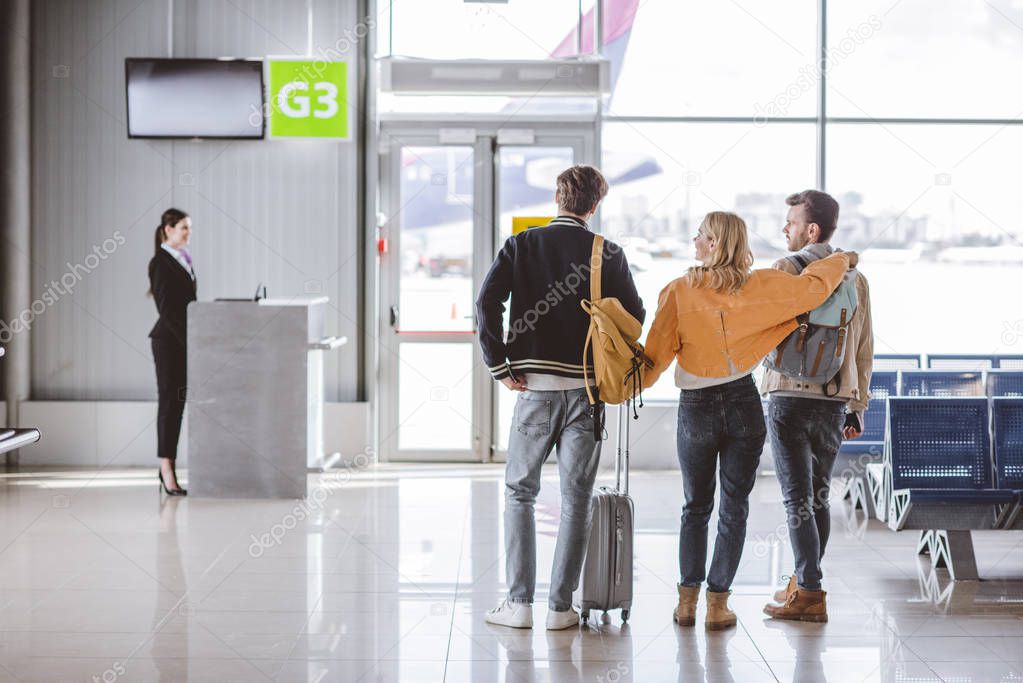 back view of young friends going to check-in desk in airport 