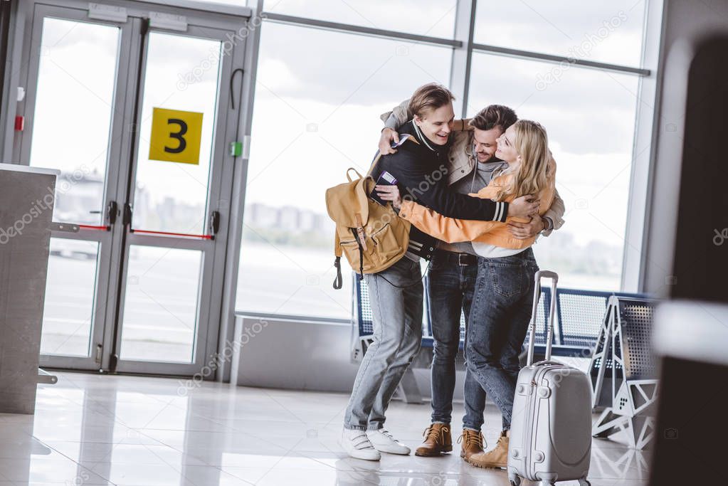 happy young friends hugging in airport terminal