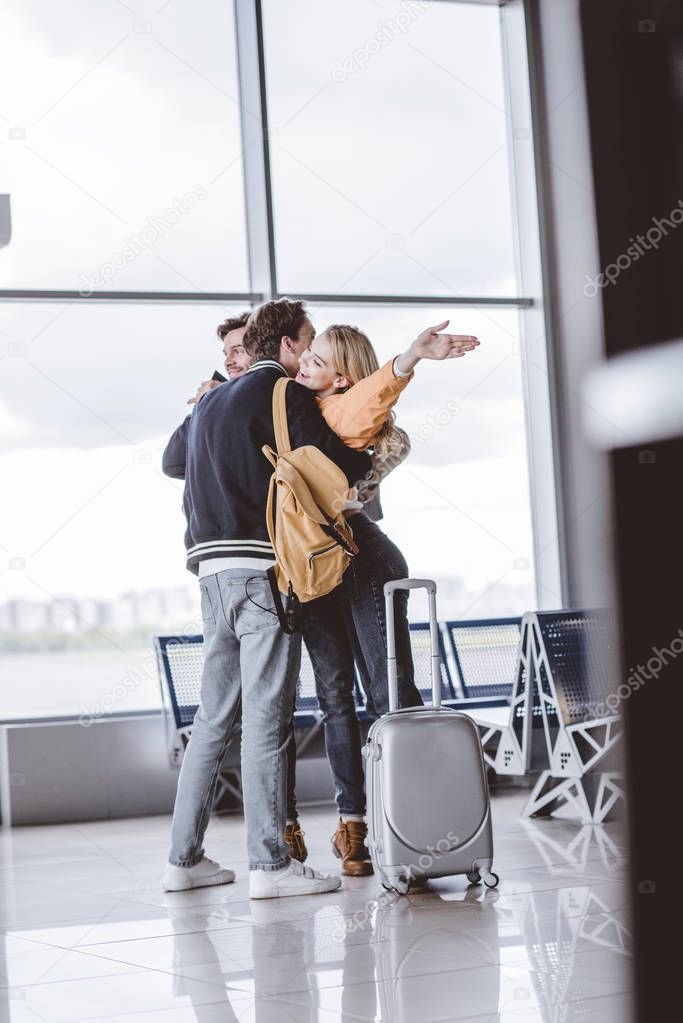 happy young friends hugging and greeting each other in airport