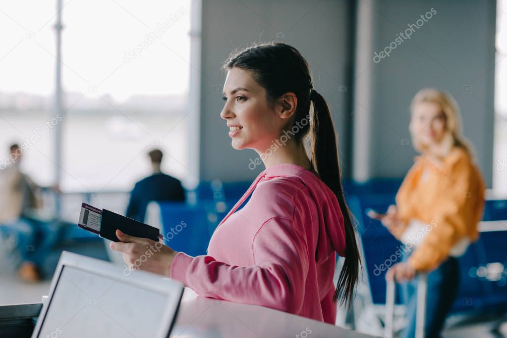 smiling young woman holding passport and boarding pass in airport terminal