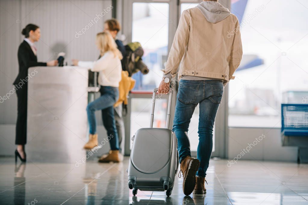 cropped shot of man with suitcase going to check-in desk in airport