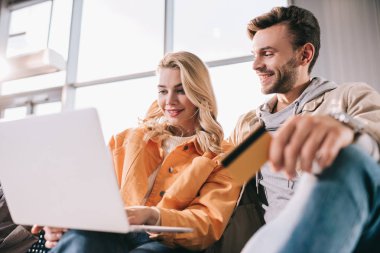 gülümseyen genç çift dizüstü beklerken Havaalanı, düşük açılı görünümü kullanma