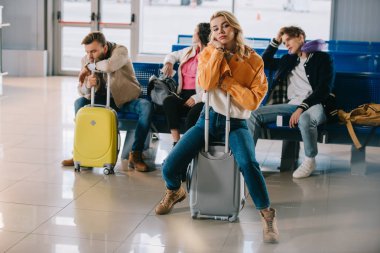 bored young people with luggage waiting for flight in airport terminal clipart