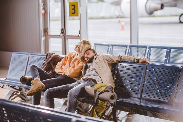 young couple sleeping while sitting together and waiting for flight in airport