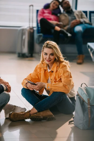 Attractive Young Woman Smiling Camera While Sitting Floor Waiting Flight — Free Stock Photo