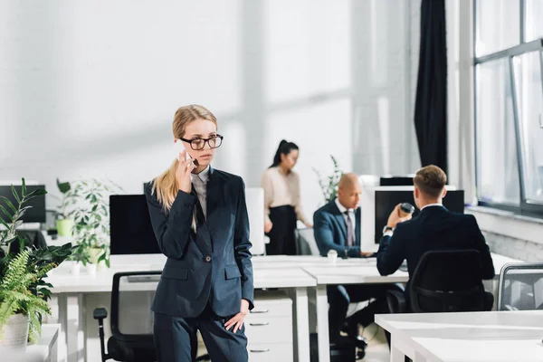 Serious Young Businesswoman Talking Smartphone While Colleagues Working Open Space — Free Stock Photo
