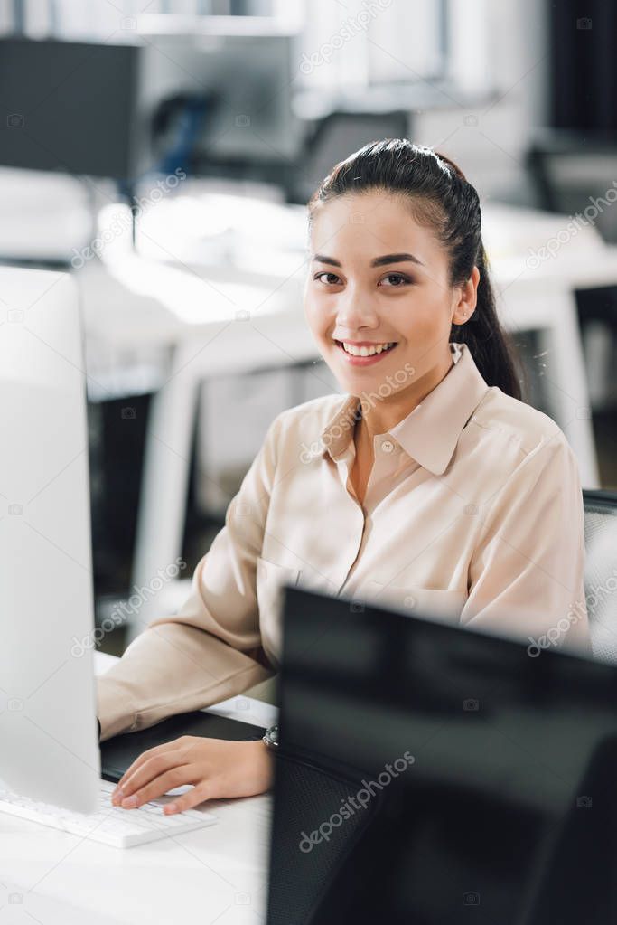 beautiful young businesswoman using desktop computer and smiling at camera in office 