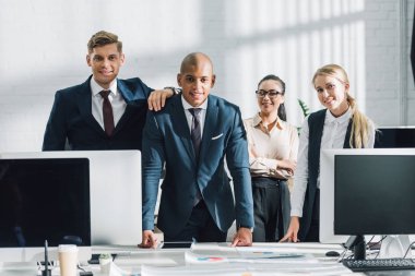 professional young multiethnic business people standing together and smiling at camera in office clipart