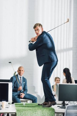 genç işadamı Golf ve arkasında ofisinde oturan arkadaşları oynuyor