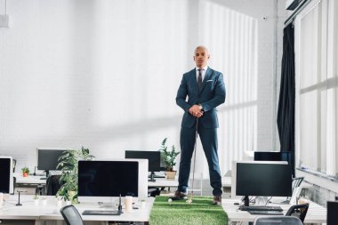 masanın üzerinde duran ve Office golf oynarken kameraya bakarak kendine güvenen genç Afro-Amerikalı işadamı 