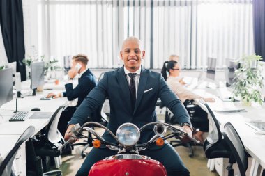 Kırmızı motosiklet sürme ve kamera Office gülümseyen mutlu genç Afro-Amerikalı işadamı  