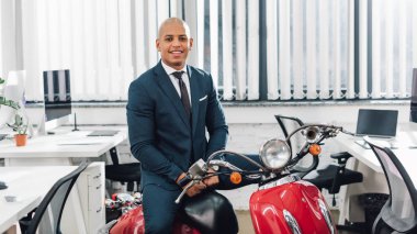 Kırmızı motosiklet üzerinde oturan ve kamera Office gülümseyen mutlu genç Afro-Amerikalı işadamı  