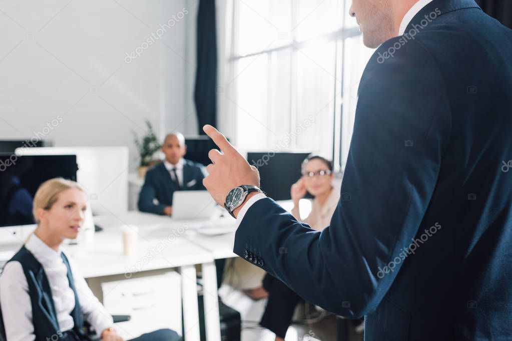 cropped shot of young businessman gesturing and talking with colleagues in open space office