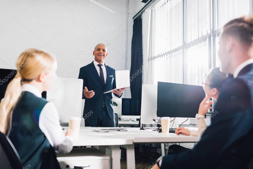 low angle view of smiling young african american businessman looking at coworkers in office 