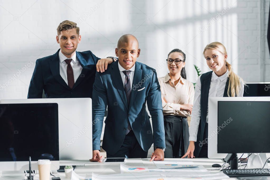 professional young multiethnic business people standing together and smiling at camera in office