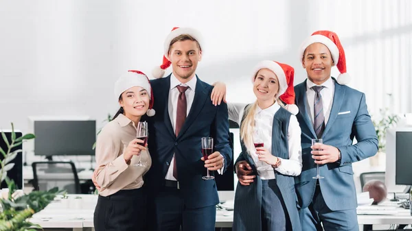 Feliz Joven Colegas Sombreros Santa Beber Vino Sonreír Cámara Mientras — Foto de Stock