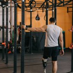 Вид сзади на молодого спортсмена с искусственной ногой, стоящего возле гимнастической лестницы в спортзале
